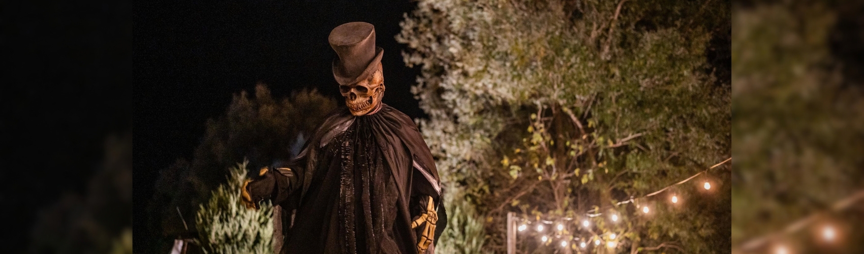 A large skeleton character in a top hat and cape at night strolling through Fear Farm.