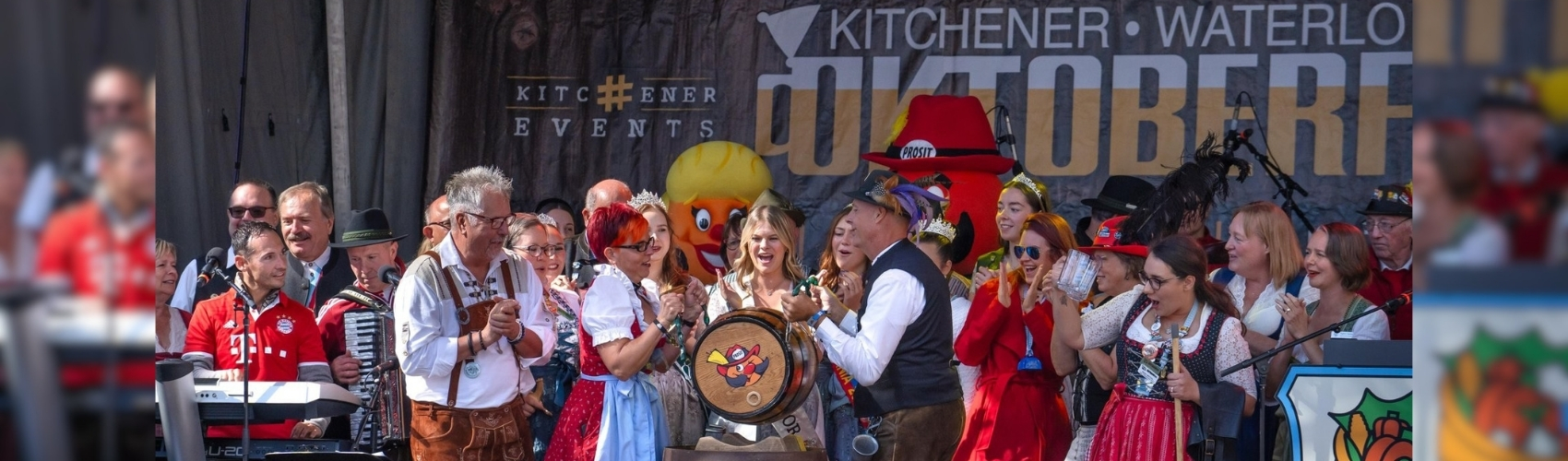 The main outdoor stage outdoors at Kitchener City Hall during the keg tapping for Kitchener-Waterloo Oktoberfest. There is a large crowd of dignitaries and Oktoberfest committee members, all wearing traditional Bavarian tracht, on stage getting ready to tap the keg.