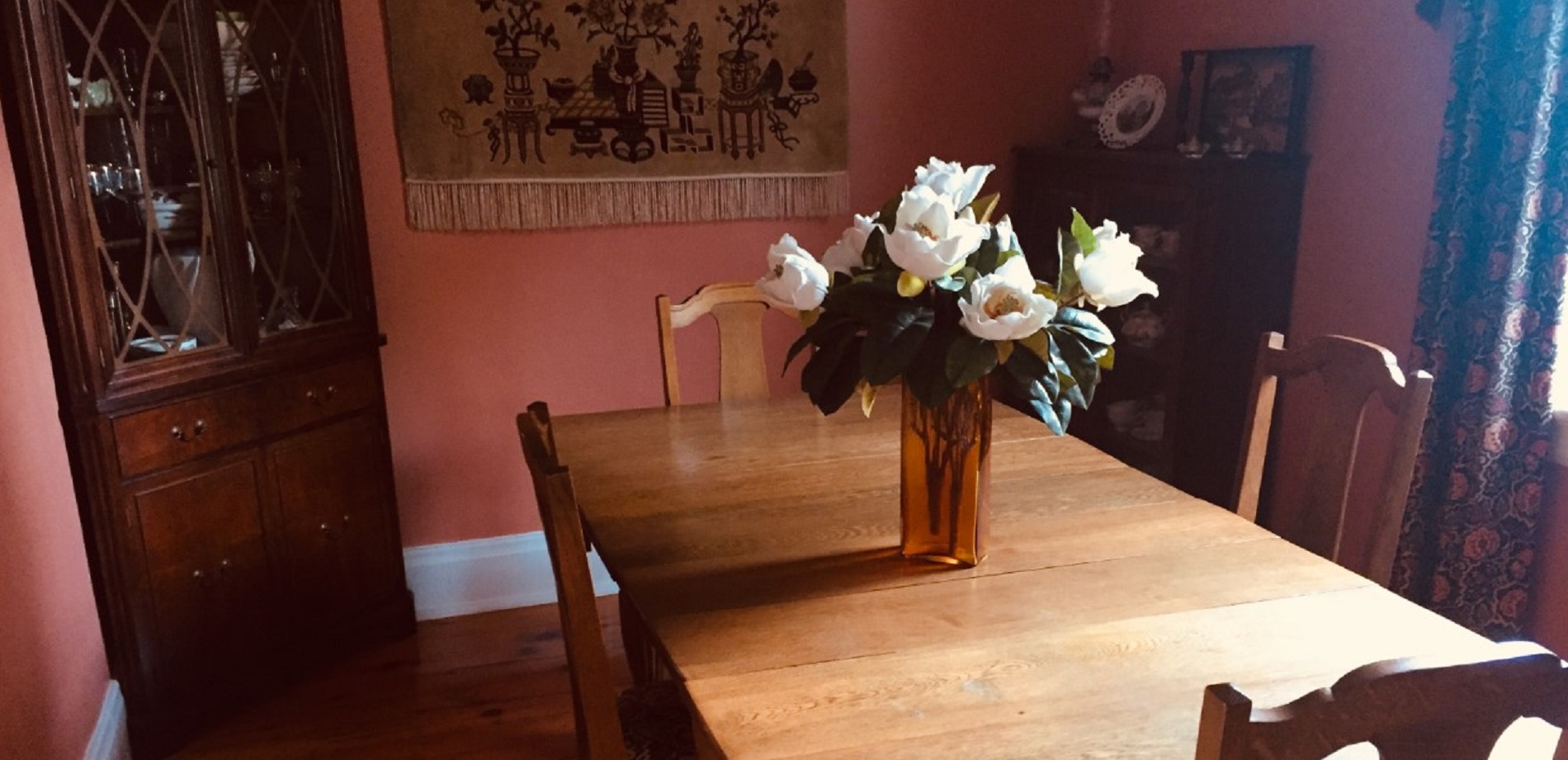 A photo of the dining area of Baumann Haus Bed & Breakfast. There are flowers on the table and the sun light shining into the room.