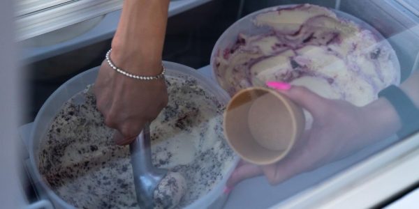 Hands reaching into a freezer display case to scoop ice cream into a cup.