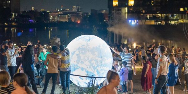 A crowd taking in a light display at Lumen in Uptown waterloo. The displays are situated along the boardwalk along Waterloo's Silver Lake: it is night.