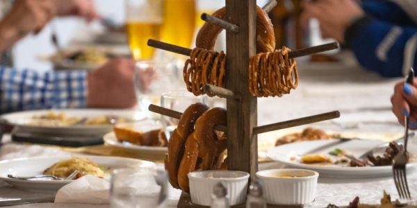 A long table of diners eating a meal. There is a stand holding large pretzels in the middles of the table: it appears to be an Oktoberfest meal.