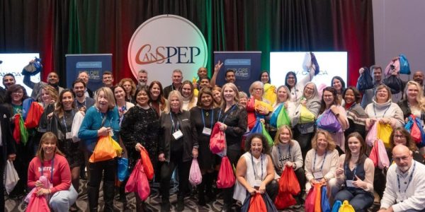 The Explore Waterloo Region Business Development team standing together with a large group of people who are all holding bags to be donated to a Toronto Charity at a holiday CanSPEP and MPI event.