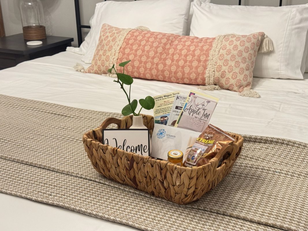A welcome basket filled with treats and pamphlets on a nicely made bed at a cozy bed and breakfast.