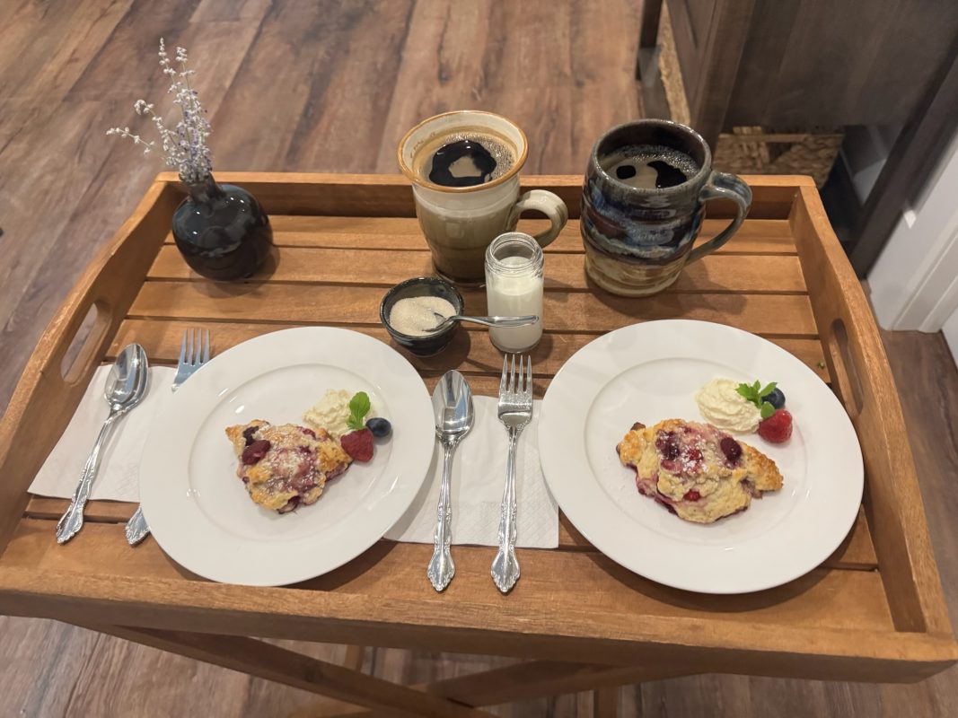 Two white plates with berry scones on them, sitting on a wooden tray. 