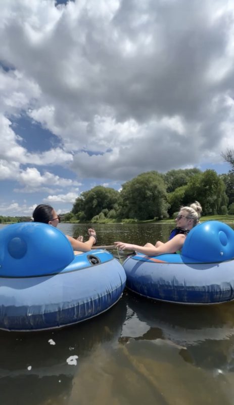 Two people floating down the Grand River in tubes with comfortable backs on them for relaxing. It is a sunny summer's day.