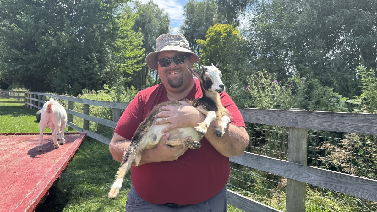 A smiling man holding a little goat at The Perth Farmhouse - Wine and Cider