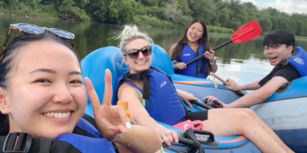 Four people in tubes with paddles on the Grand River. They are smiling, and it is a sunny summer's day