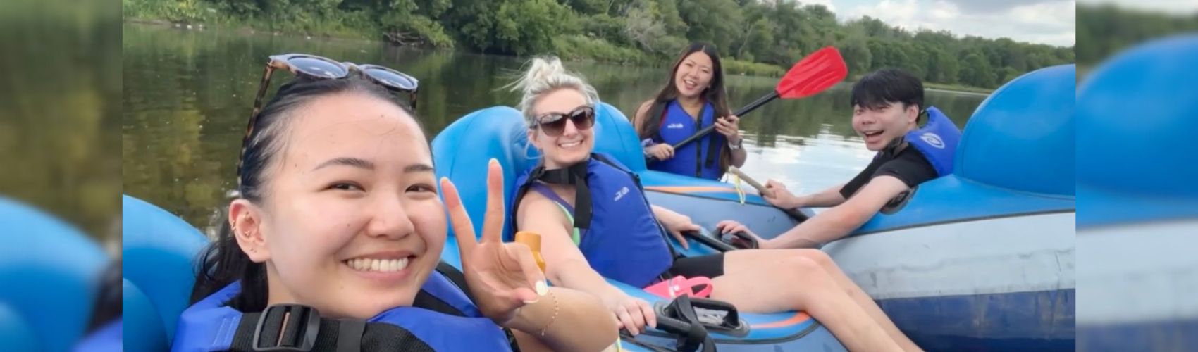 Four people in tubes with paddles on the Grand River. They are smiling, and it is a sunny summer's day