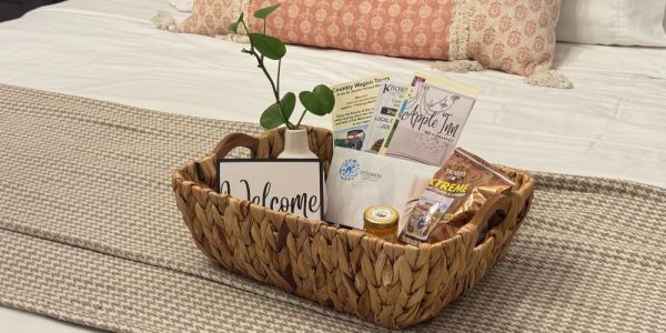 A welcome basket filled with treats and pamphlets on a nicely made bed at a cozy bed and breakfast.