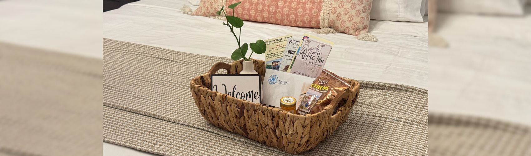 A welcome basket filled with treats and pamphlets on a nicely made bed at a cozy bed and breakfast.