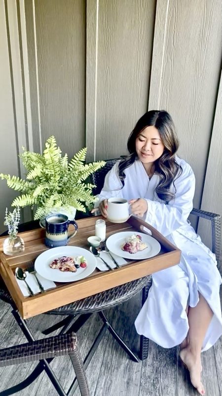 A guest sitting with a breakfast tray on a table beside her with two plated breakfasts on it, at Apple Inn Bed and Breakfast.