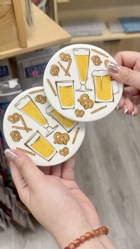 Hands holding a couple of coasters with drawn beer steins and pretzels on them
