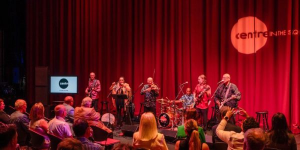 An intimate concert taking place on the main stage at Centre in the Square in Kitchener. The audience is also on the stage taking in the performance by 5 musicians.