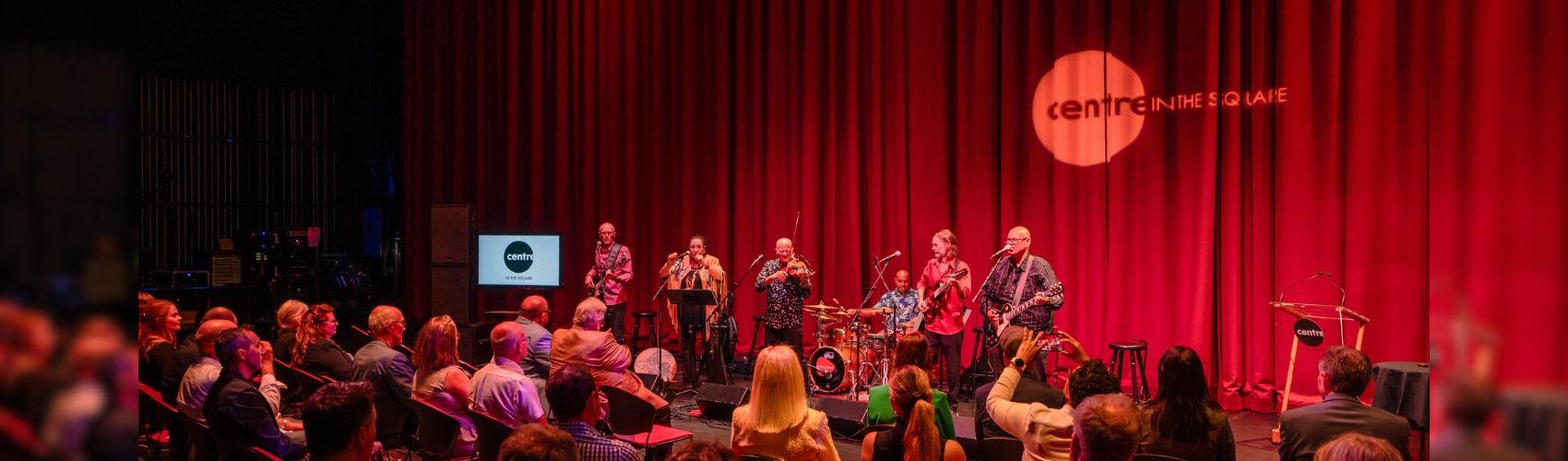 An intimate concert taking place on the main stage at Centre in the Square in Kitchener. The audience is also on the stage taking in the performance by 5 musicians.