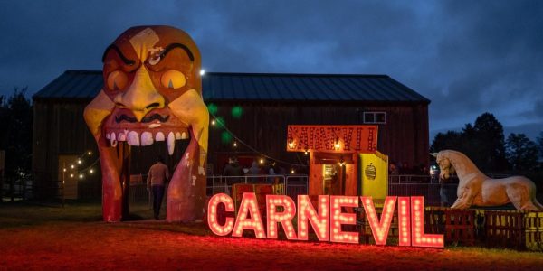 An entrance to Snyder's Farm's Fear Farm. It looks like a large, evil demon's open-mouthed smiling head, with the word CARNEVIL in large letters beside it. It is dusk.