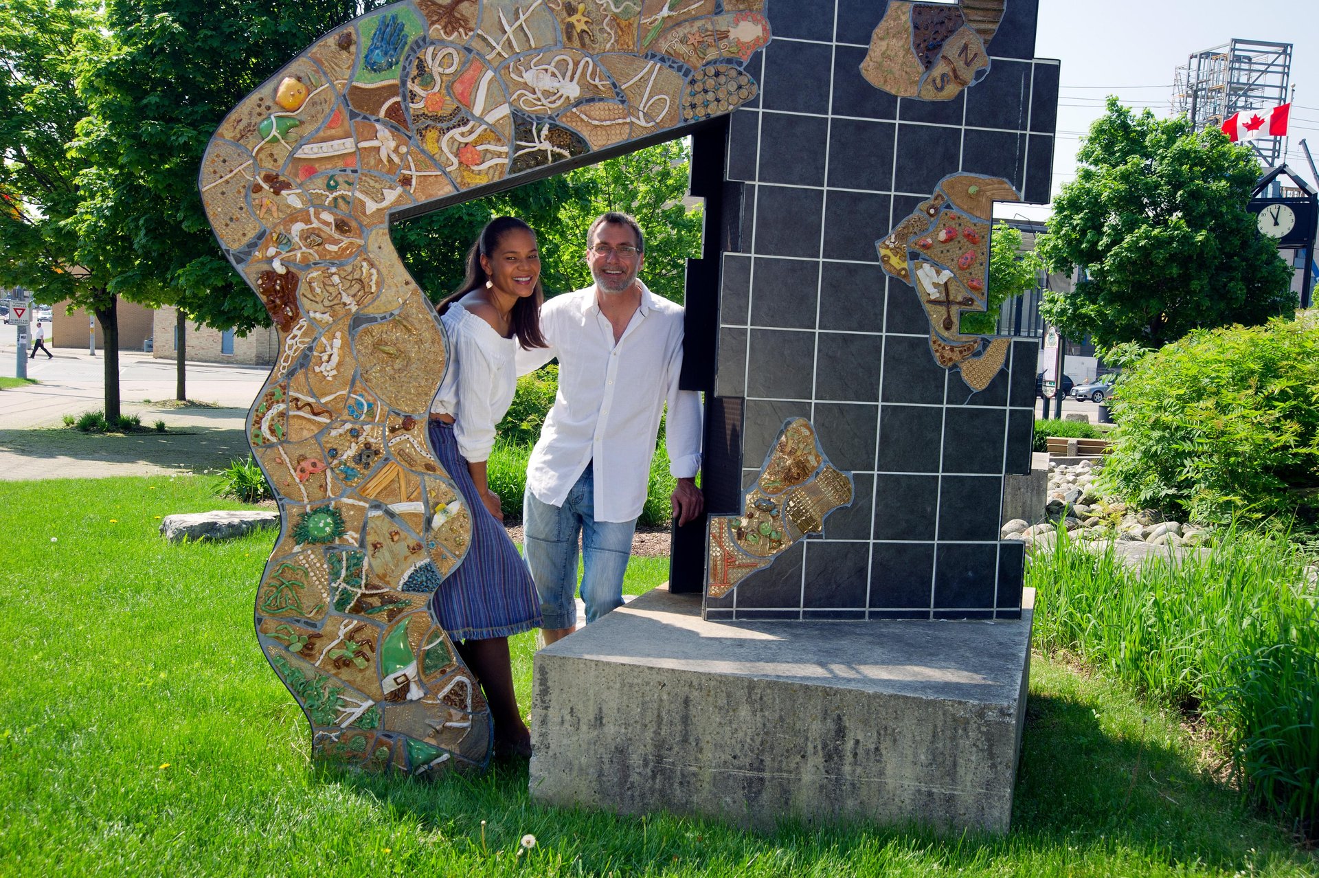 Two people posing around a large outdoor sculpture piece at the Canadian Clay and Glass Gallery in Waterloo. It is a sunny summer's day.