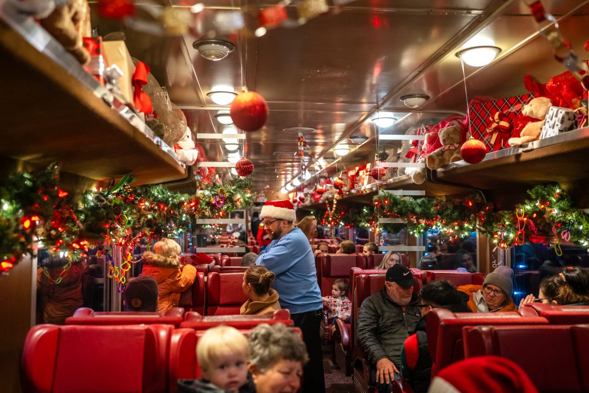 The festive train car of the Waterloo Central Railway during one of its annual Holiday rides. The car is decorated with lots of garlands and holiday decor. The is a man in a Santa hat handing things out to passengers.