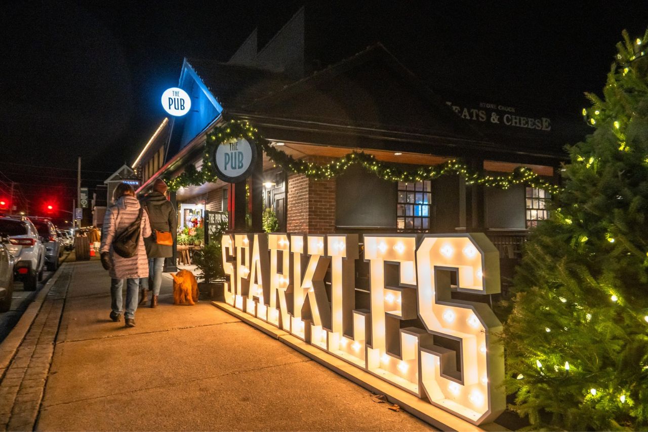 Downtown St. Jacobs during the annual Sparkles event. A person is walking past large, lit-up letters that spell Sparkles. The St. Jacobs Pub is in the background.