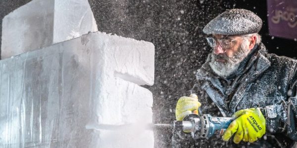 A snow carver working on a piece on the street during Winterloo. It is dark out, and it appears to be cold.
