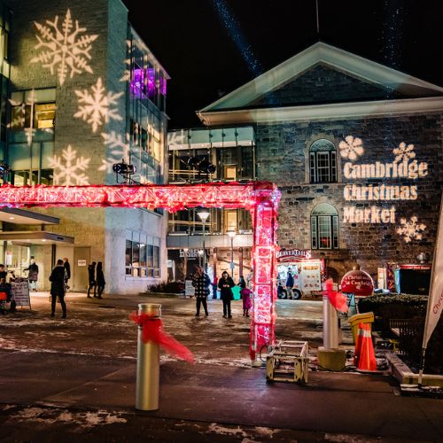 The outdoor entrance of the Cambridge Holiday Market at the Cambridge City Hall. It is night, and there are holiday lights shining.