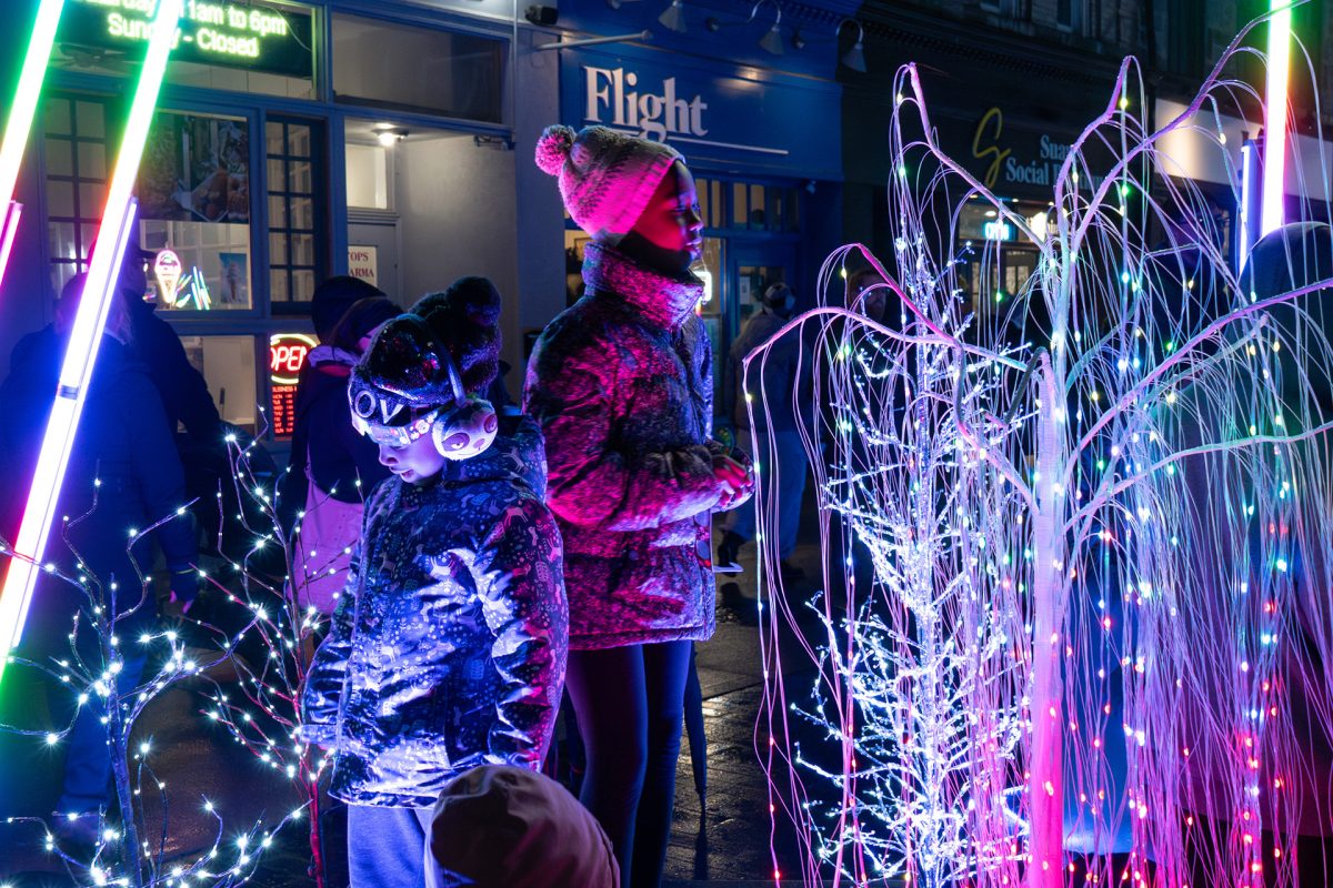 A group of people bundled up for winter and looking at outdoor holiday light displays
