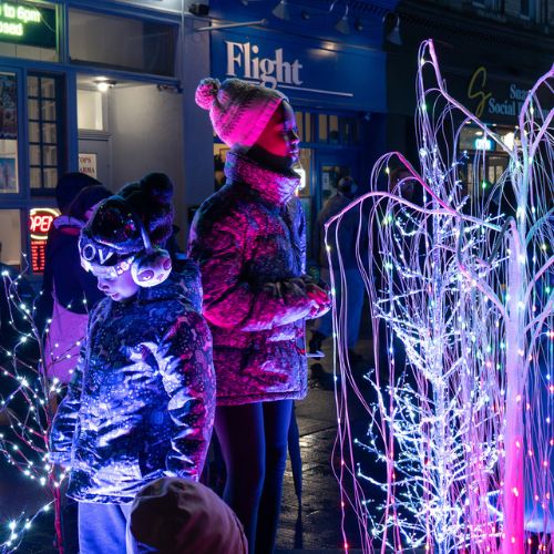 A group of people bundled up for winter and looking at outdoor holiday light displays