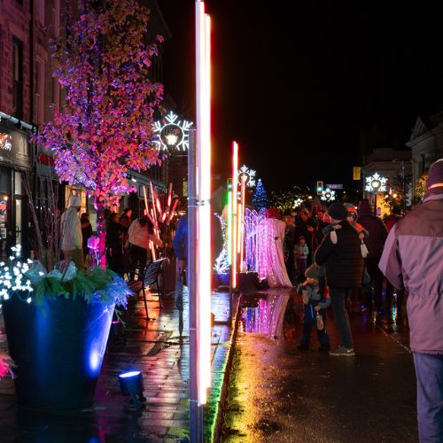 A large crowd of people walking down the streets of downtown Cambridge at night. It is winter: they are participating in the annual Phil Klein's Unsilent Night event.
