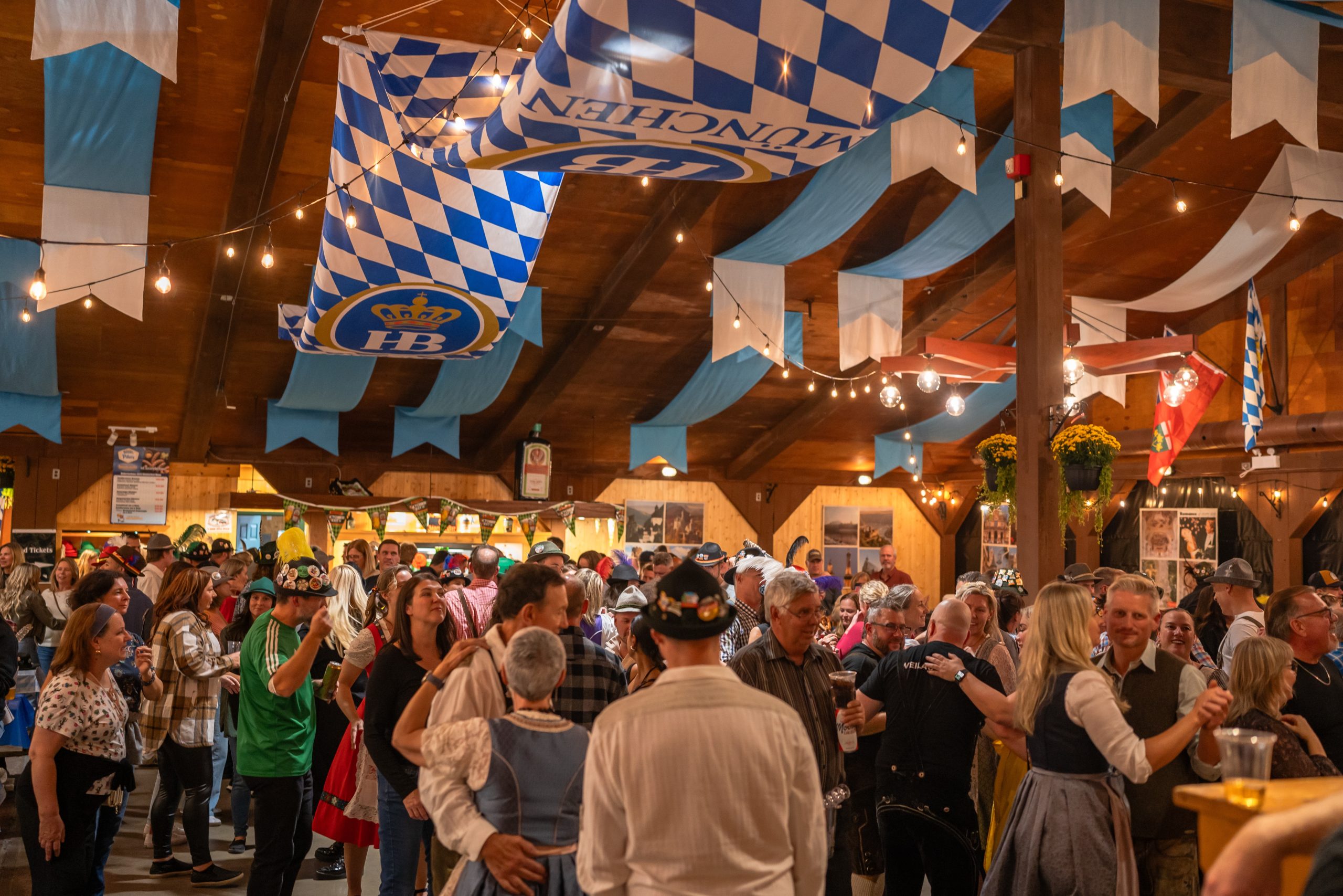 A large group of people dancing in a traditional festhalle during Kitchener Waterloo Oktoberfest. Many are dressed in traditional Bavarian costumes.