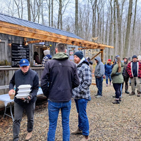 A line up of people waiting to participate in a pancake breakfast in Sand Hills Maple Products' sugar bush.