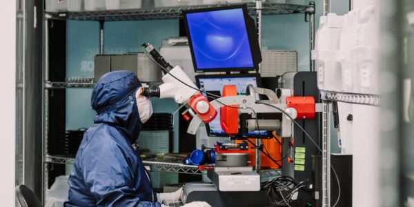 An employee in protective gear looks through a microscope in a lab at Teledyne DALSA in Waterloo