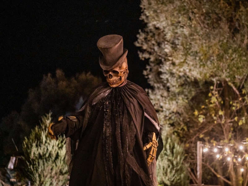 A large skeleton character in a top hat and cape at night strolling through Fear Farm.