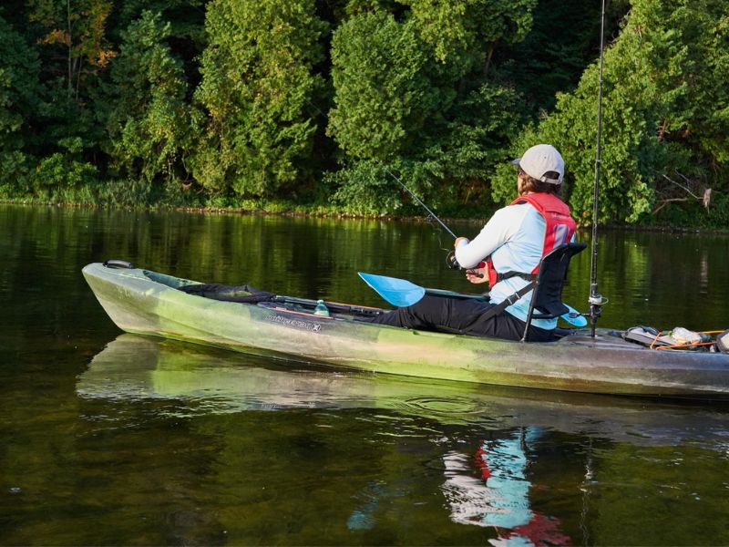 a kayaker paddling on the Grand River. It is a sunny summer's day: the shoreline is lined with large, green trees and vegetation.