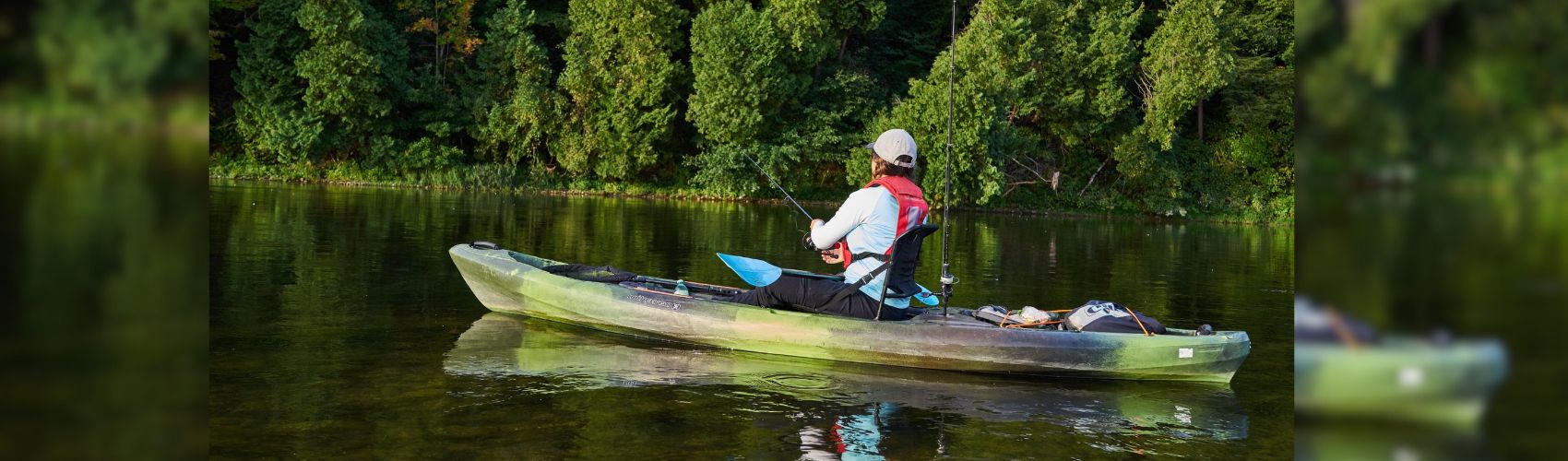 a kayaker paddling on the Grand River. It is a sunny summer's day: the shoreline is lined with large, green trees and vegetation.