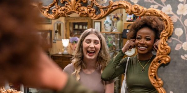 Two friends looking into a vintage gold-filagreed mirror in a vendor stall at Market Road Antiques in St. Jacobs.