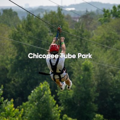 A person going down the zipline course at Chicopee Tube Park in Kitchener. It is summer, and you can see the green canopy of mature trees beneath them.