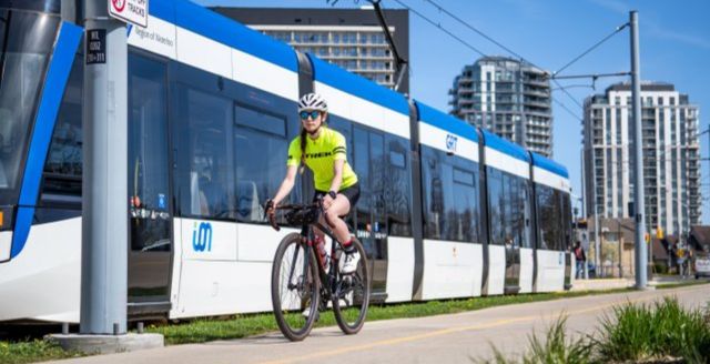 A cyclist riding beside an ION Light Rail Transit train as it travels through Waterloo on a sunny summer's day.