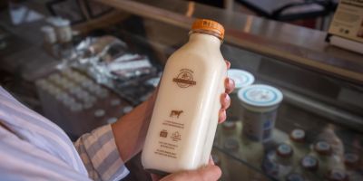 A person holding a glass bottle of milk from Eby Manor Farm. The person appears to be in Eby Manor's on farm store. 