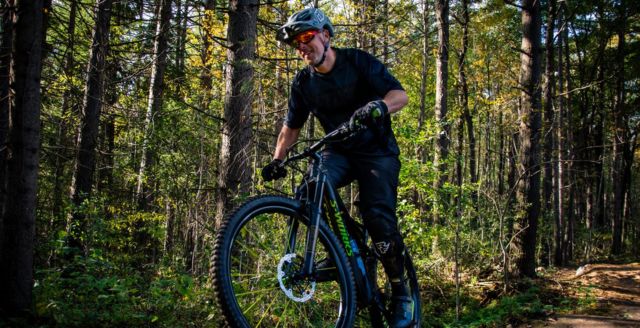 A cyclist on  a mountain bike riding one of the forest trails along the Hydrocut Trail in Waterloo Region. It is a sunny summer's day: you can see the sun through the trees.