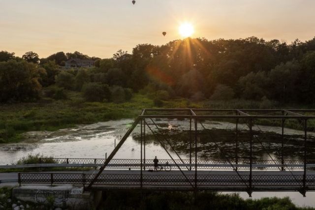 A cyclists on an iron bridge over a river watching a sunset in the countryside