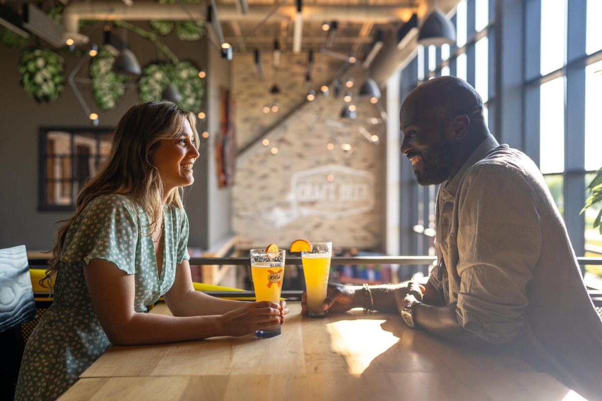 A couple sitting at a sunny table inside the taproom at Waterloo Brewing. They are smiling and drinking a craft beer together.