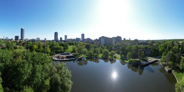 A drone view of the City of Kitchener that shows Victoria Park, Victoria Park Lake, the high rise buildings in downtown Kitchener, and many green trees throughout.