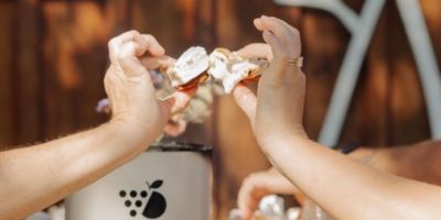 A close up of two hands, both holding s'mores, and meeting together as in a 'cheers' fashion.