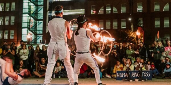 Two buskers performing in the streets of Uptown Waterloo in the evening. One is juggling flames, the other is throwing and catching lit up hoops.