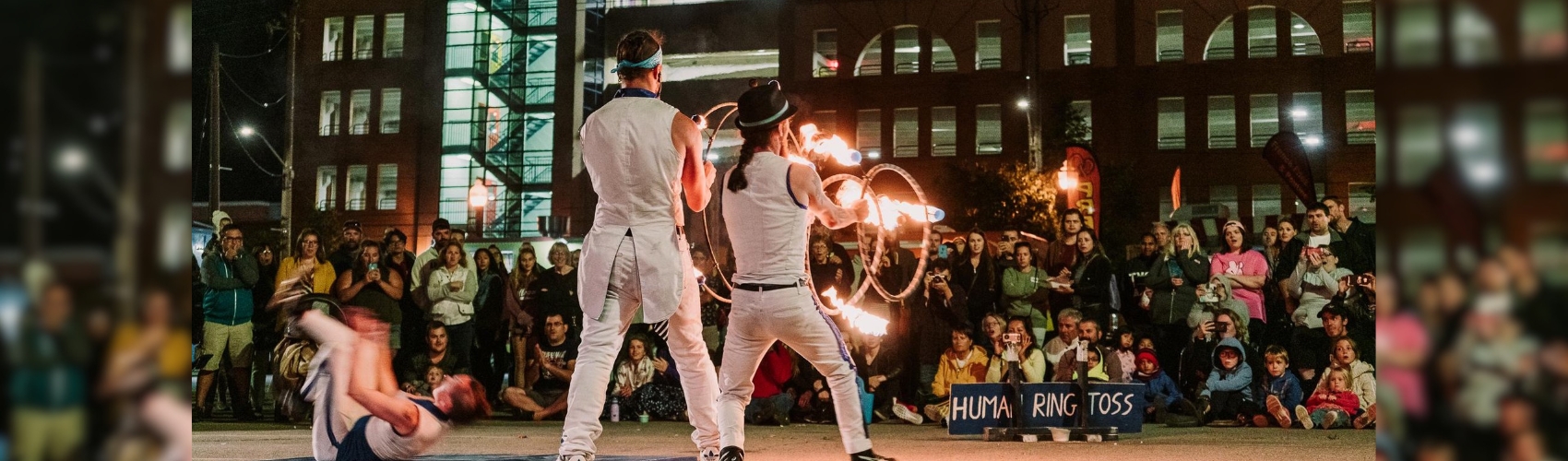 Two buskers performing in the streets of Uptown Waterloo in the evening. One is juggling flames, the other is throwing and catching lit up hoops.