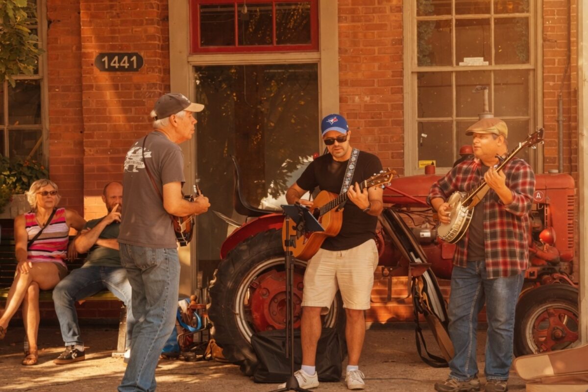 Three performers playing guitars and banjo on the street corner in St. Jacobs during the annual Bales and Boots fall event in the village.