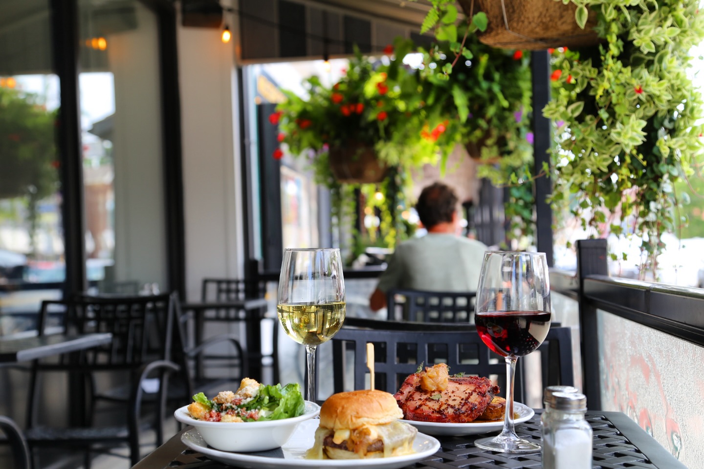 The patio at Jacob's Grill in St. Jacobs on a sunny day. You can see a table with two glasses of wine and two plated entrees on it. In the background you can see other diners enjoying a meal. 