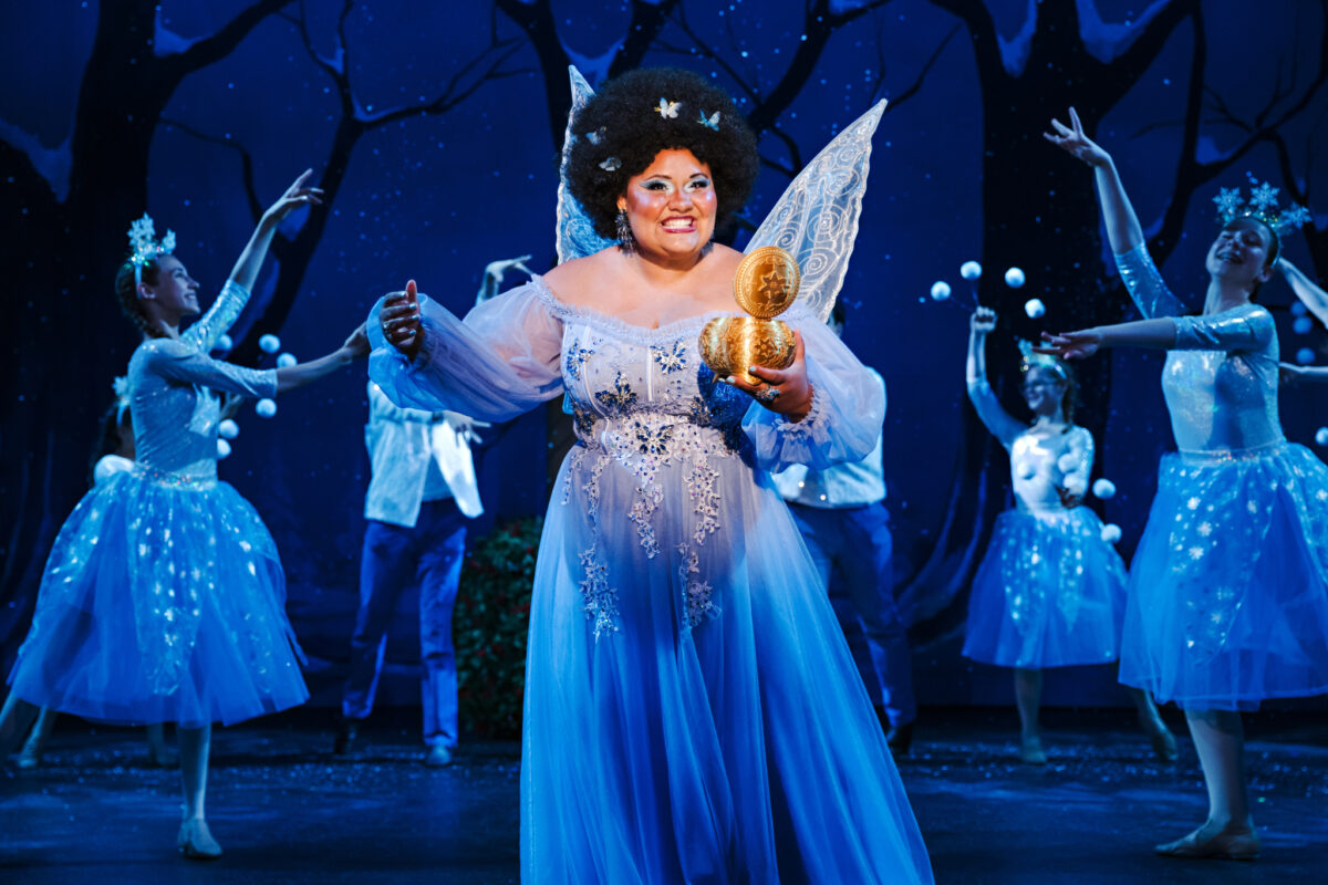 Drayton Entertainment production photo of Snow White - the Panto. There is a person dressed as a large fairy in the foreground, with other fairies dancing behind them on stage.
