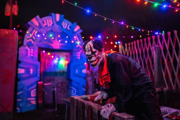 A scary looking, leering clown is poised outside of one of the haunted attractions at Screampark at night.
