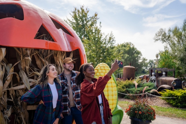 Three people taking a selfie in front of a giant jack-o-lantern display at Snyder's Farm. It is a sunny fall day.
